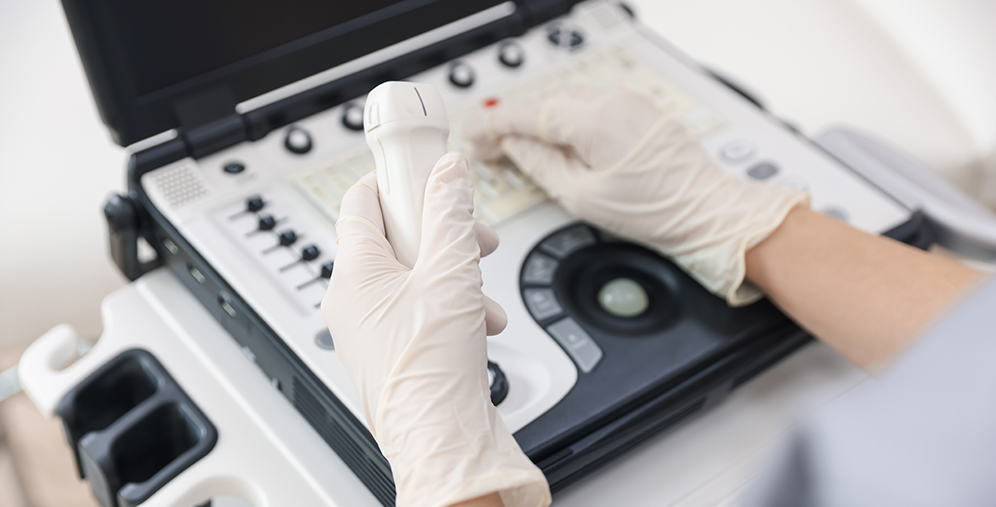 Medical professional wearing gloves holds an ultrasound transducer while operating an ultrasound machine.