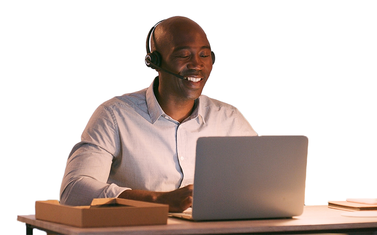 Customer service agent with headset smiling at a laptop on a desk, a small box nearby.