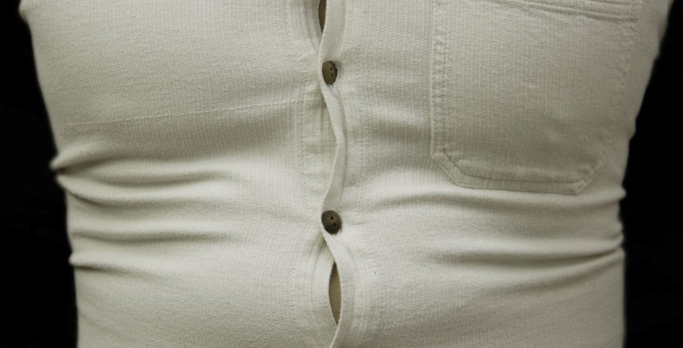 Close-up of a cream ribbed button-up shirt with buttons undone along the front, exposing a small opening at the waist.