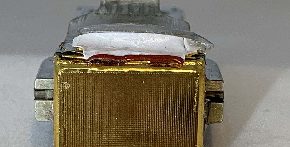 Close-up of a gold rectangular electrical component mounted in a metal frame with white insulating material on top.