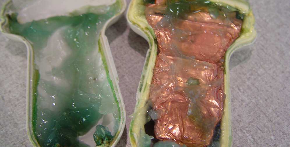 Cross-section of a green and yellow capsule-like object; left side shows green gel, right side has copper-colored foil-wrapped material.
