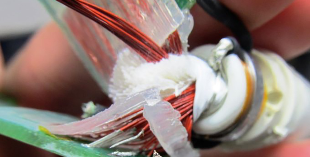 Close-up of a frayed electrical cable with exposed copper strands and torn insulation.